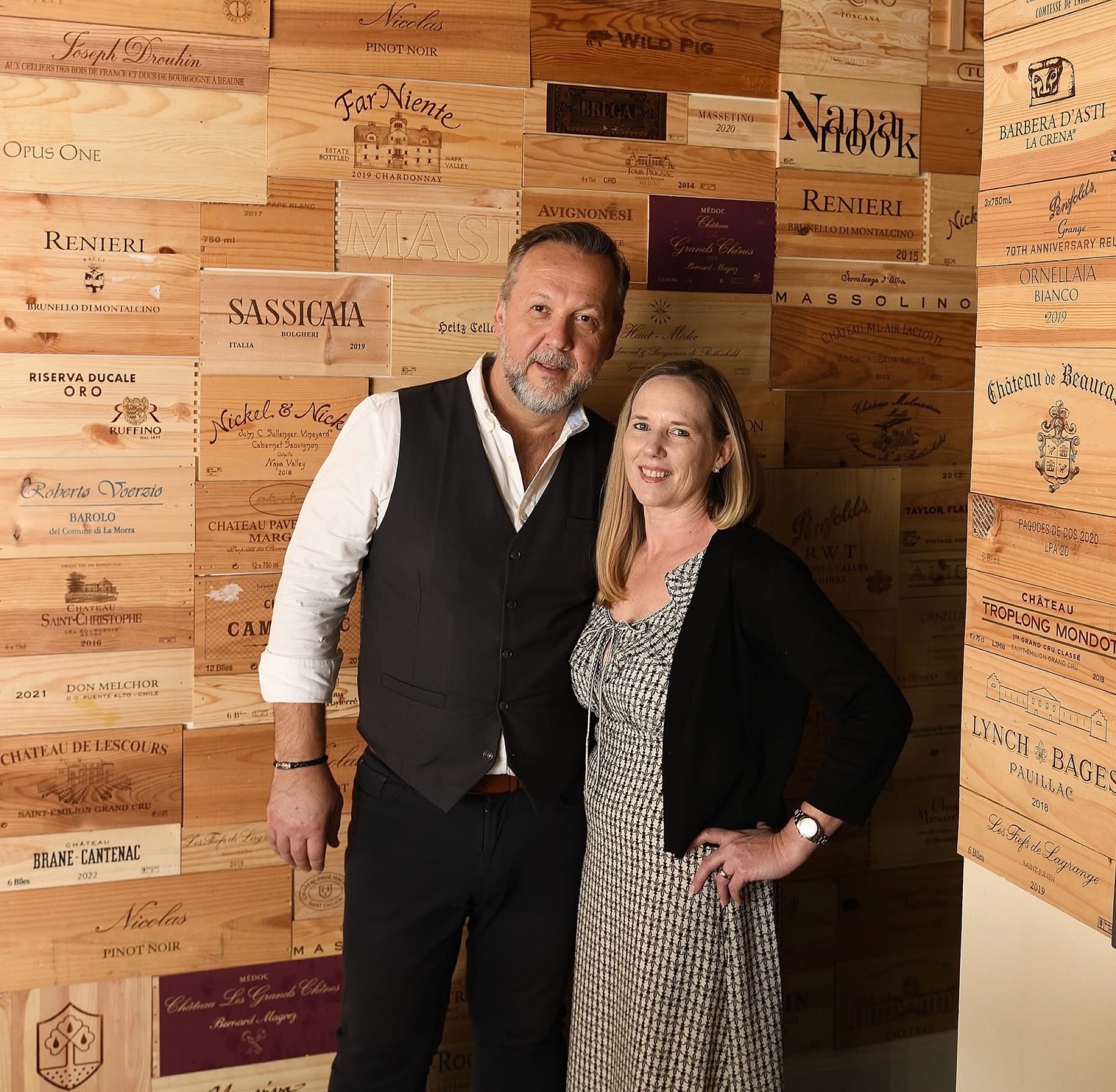 The owners of Vinea in front of a wall of European wine boxes